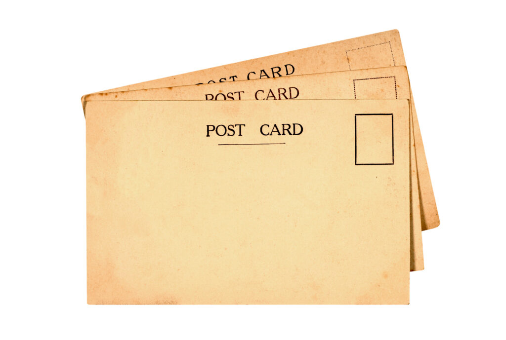 A stack of vintage postal cards with 'POST CARD' printed at the top and space for a stamp on the right, displaying an aged, nostalgic look, with postal codes such as 10001, 94105, and 560001 faintly visible in the background.