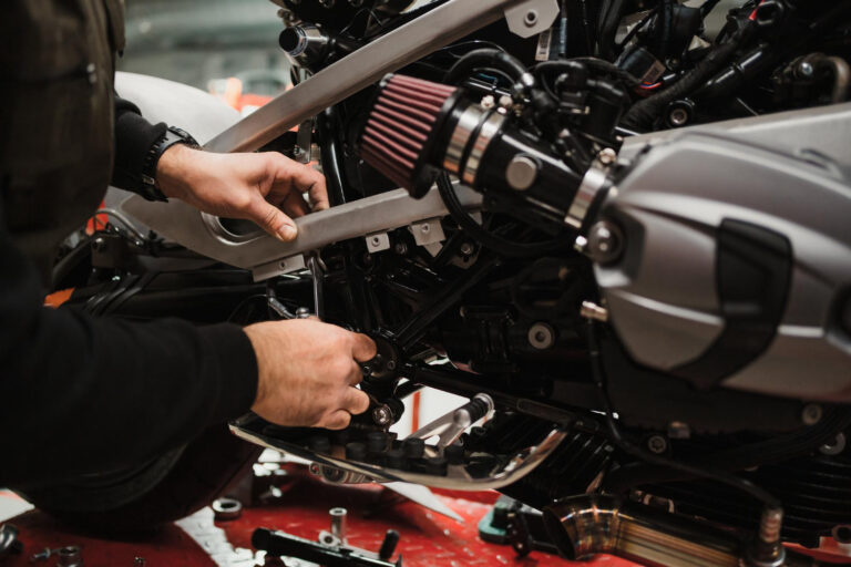 Best bike engine oil: A motorcycle mechanic is carefully adjusting a component on a motorcycle engine. Tools and parts are scattered around the workspace.